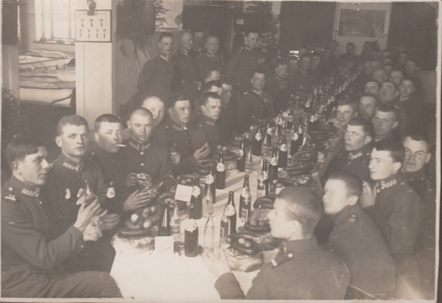 Wspólny posiłek przy świątecznym stole w budynku koszarowym. Na stole widoczne pieczywo, kiełbasy, gotowane jajka i alkohol, lata 20. – 30. XX w. (MWB/D/443)