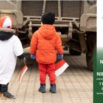 Baner. Dzieci podziwiają maszynę wojskową. Dzieci obrane w barwy narodowe