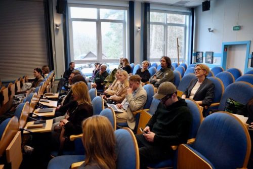 Uczestnicy siedzą na sali konferencyjnej.