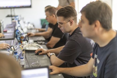 Mężczyzna pracuje na komputerze, siedzi w środku innych osób.